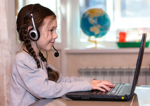 Home distance learning. A little schoolgirl sits at a laptop and does homework, or listens to a teacher. Online education.