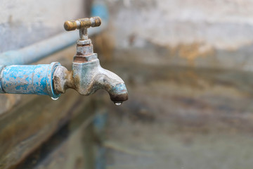 Water dripping from old bass faucet connect to the blue pvc pipe flowing into water surface of bath made of cement close-up.