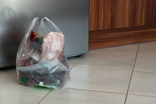 A Bag Of Plastic Trash In The Kitchen In Front Of The Fridge On The Ground.