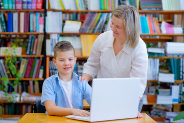 Fototapeta na wymiar Teacher and school boy using laptop in library at school