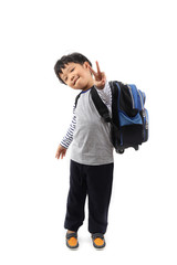 A cheerful Asian primary schoolboy with a backpack showing victory gesture sign isolated on white background.