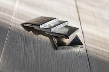 Mini chocolate bars in silver paper on white wooden background. Natural cocoa product in portion...