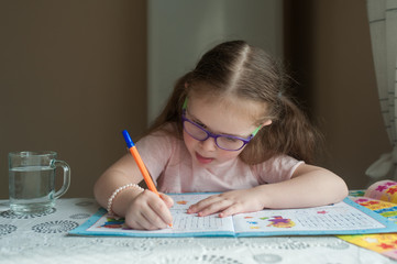 Happy pretty child girls sitting at the table and writes. Educational activities at home. Distance learning. Girl with glasses. Vision problems
