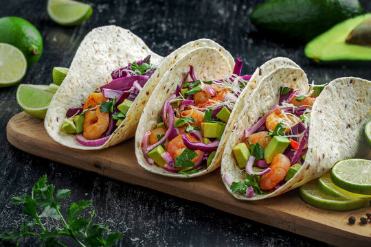 Tacos with shrimps., avocado and red onion on a wooden table. Traditional American fast food.