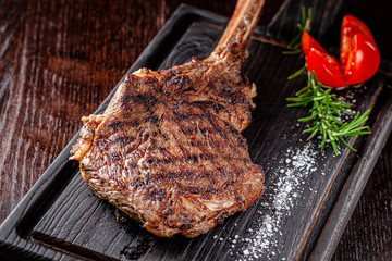 American cuisine. Large juicy grilled steak on a tomahawk bone. Beef steak on a wooden board with...