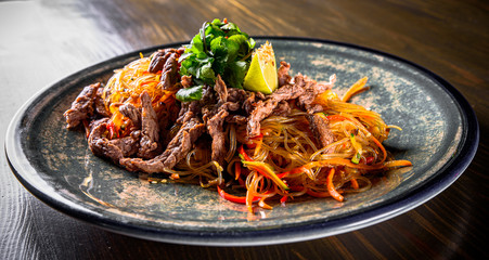 Udon stir-fry noodles with beef meat, vegetables and sesame in plate on wooden table background
