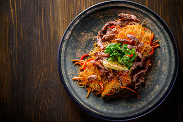 Udon stir-fry noodles with beef meat, vegetables and sesame in plate on wooden table background