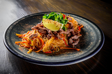 Udon stir-fry noodles with beef meat, vegetables and sesame in plate on wooden table background