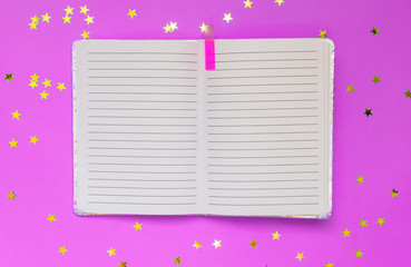 Open empty notebook on a pink background with stars confetti. Top view. Space for text or design