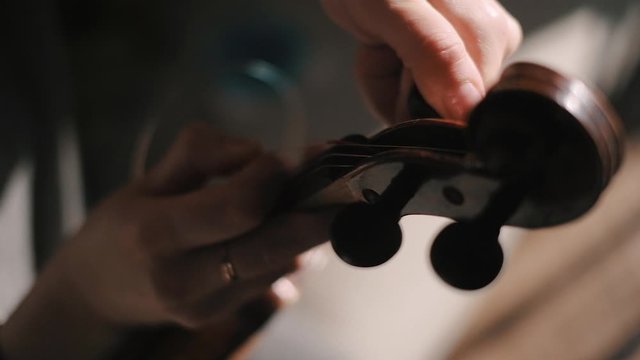 Young woman fiddler changing violin strings, tighten the string with the tuning peg at pegbox, moody low light scene at home