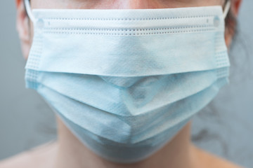 Close-up woman wearing a face surgical mask on gray background. Selective focus. Flu, illness, pandemic concept