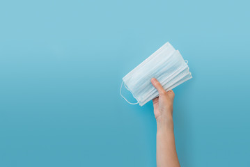 Hand holding wearing mask on blue background.  Flu, illness, pandemic concept