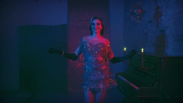 Young beautiful happy retro woman smiling in bright sparkling luxury sexy gold dress in 20s style, finger wave hairstyle dancing in room near piano candles burning neon light. Vintage style of party