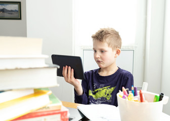 Caucasian preteen boy concentrated on his task with tablet with books and copybooks around. Concept of distance learning in isolation