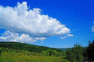 Panoramic view of the Carpathian mountains covered by a green forest under a blue sky and white clouds