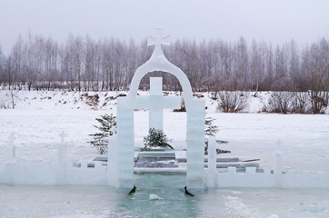Cross carved from ice on a winter lake near the ice hole at Epiphany on a frosty day