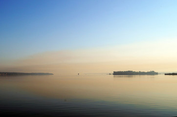 View of the lake with mirrored calm water covered in fog on a cool summer morning