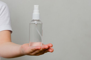Hands of a child of four years holding a bottle with a sanitizer on a gray background