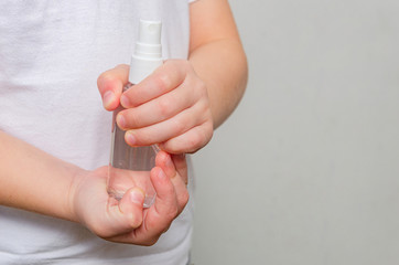 Hands of a child of four years holding a bottle with a sanitizer on a gray background.