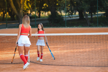 Obraz premium Little girl and her mother playing tennis on court