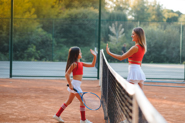 Little girl and her mother playing tennis on court