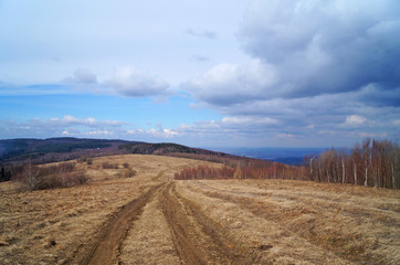 View of autumn mountains with trees without leaves under a cold gray sky and heavy white clouds