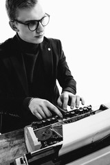 A young male journalist with glasses near a typewriter.