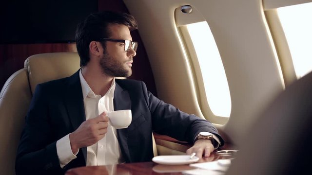 businessman holding coffee and looking in illuminator while traveling by plane