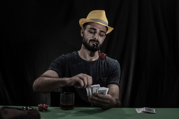 Portrait of young brunette Indian/European/Arabian/Kashmiri man in casual tee shirt throwing casino chips on a casino table in black copy space studio background. lifestyle and fashion.