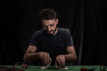 Portrait of young brunette Indian/European/Arabian/Kashmiri man in casual tee shirt throwing casino chips on a casino table in black copy space studio background. lifestyle and fashion.