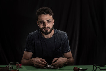 Portrait of young brunette Indian/European/Arabian/Kashmiri man in casual tee shirt throwing casino chips on a casino table in black copy space studio background. lifestyle and fashion.