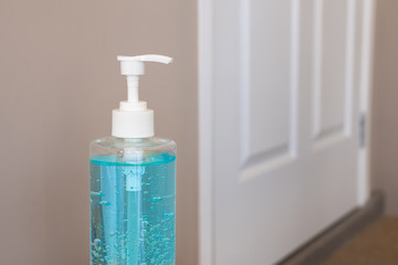 Blue hand sanitizer gel in clear pump bottle lay in front of home door, that use for killing germs, bacteria and viruses. Prevent the spread of germs and bacteria and avoid infections corona virus.