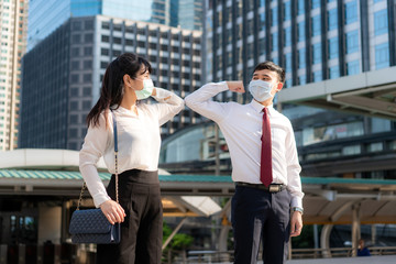Elbow bump is new novel greeting to avoid the spread of coronavirus. Two Asian business friends meet in front of office building. Instead of greeting with a hug or handshake, they bump elbows instead.