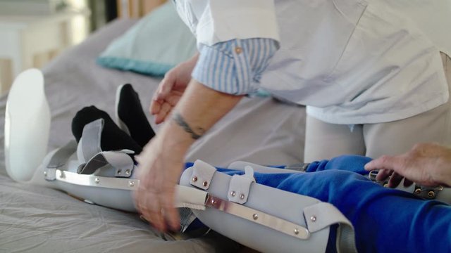 Healthcare worker and paralysed senior patient in hospital, applying orthosis.