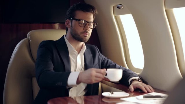 confident businessman drinking coffee while traveling by plane