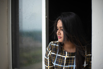 Portrait of young brunette Indian Bengali plus size woman in western wear looking outside in front of a glass window with the reflection of buildings. lifestyle and fashion.