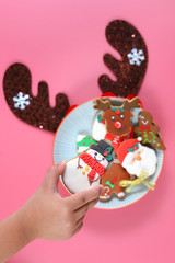 Top View Hand Holding A Snowman Shape Cookie With Icing Sugar From A Plate Isolated On Pink Background