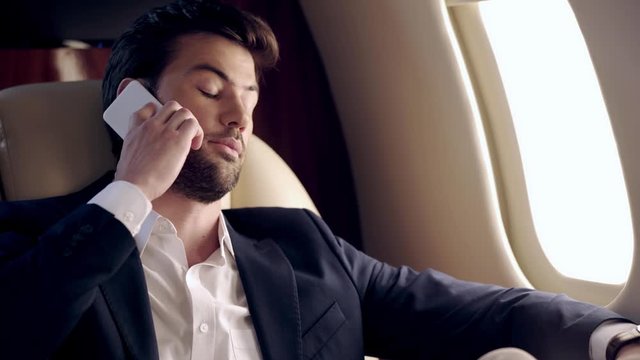 confident businessman talking on smartphone while traveling by plane