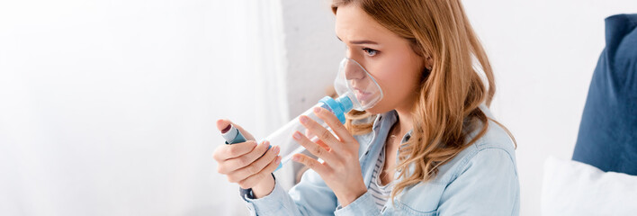panoramic shot of asthmatic woman using inhaler with spacer
