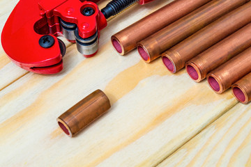 Red pipe cutter and copper pipes with connectors for plumbing repairs on wooden boards closeup