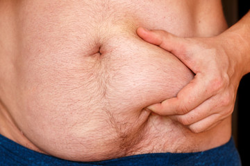Fototapeta premium A man holds his stomach with his hand and shows his fat.