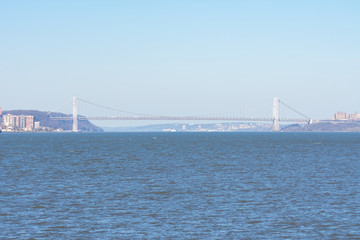 Obraz premium The George Washington Bridge in the distance over the Hudson River with a Clear Blue Sky