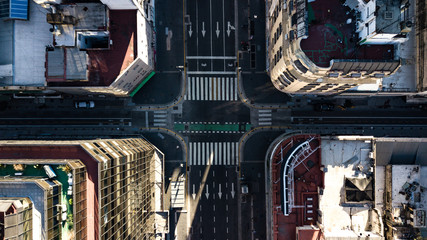 Aerial top down view on four way intersection in between tall buildings during golden hour (sunset...