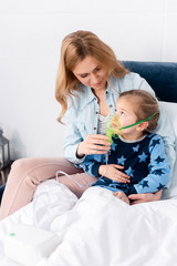 caring mother touching respiratory mask on asthmatic daughter using compressor inhaler