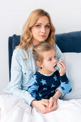 beautiful mother sitting near sick daughter using inhaler
