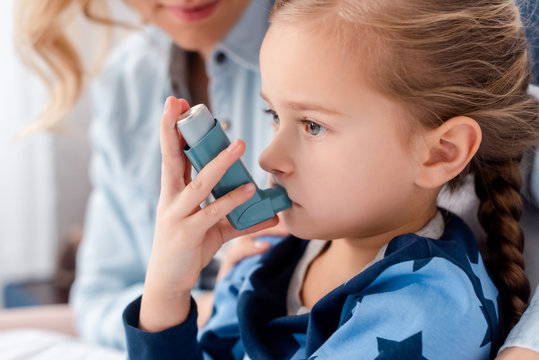 selective focus of sick kid using inhaler near caring mother at home