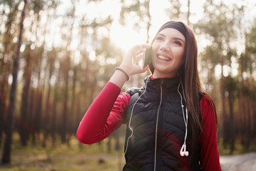 Teenager girl is walking in a pine forest at the weekend. She is talking to her friend on the phone. She has a beautiful smile. Healthy lifestyle concept.