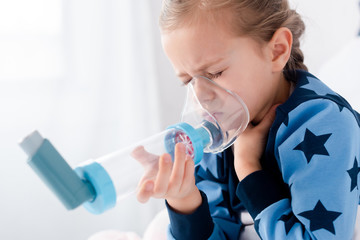 sick kid with closed eyes using inhaler with spacer