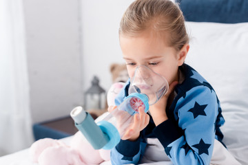 sick child using inhaler with spacer in bedroom - obrazy, fototapety, plakaty