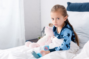 sick kid holding inhaler with spacer and looking at camera in bedroom